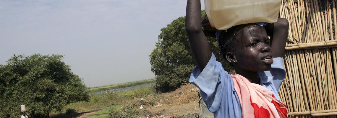 Niña africana transportando sobre su cabeza una garrafa de agua posiblemente no segura 